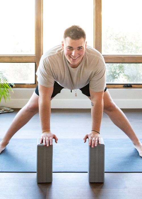 man doing yoga with 2 grey yoga blocks on a yoga mat in grey shirt and black shorts